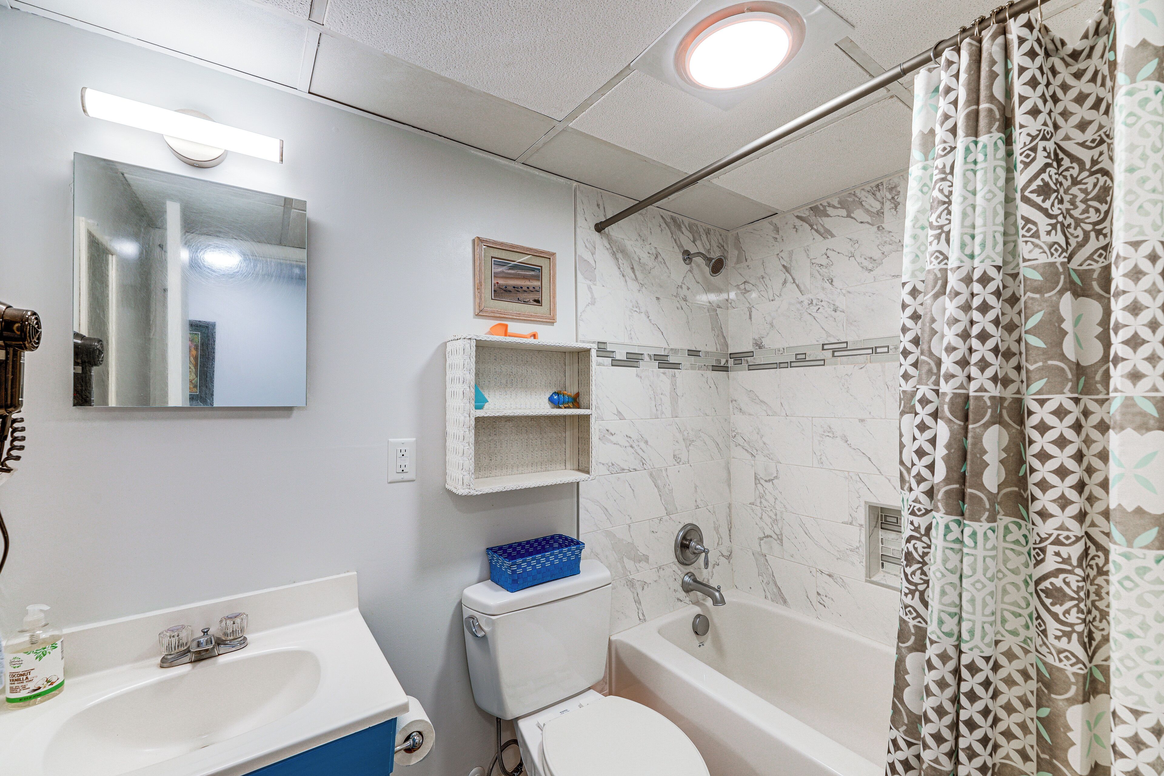 A bathroom with a white sink, toilet, and bathtub, marble walls, and patterned shower curtain.