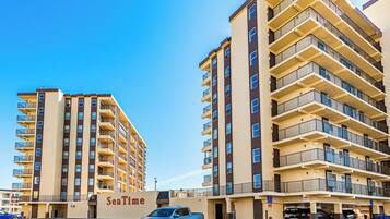 Un hotel de varios pisos con balcones, un área de estacionamiento y cielo despejado.