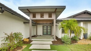 A modern house with a front porch, a door, and a small garden with plants and a palm tree. - Luxe Canal Home 2 King Suites Huge Salt Pool (Punta Gorda)