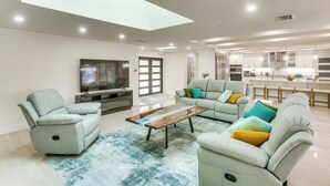 A modern living room with a flat-screen TV, a sofa set, a coffee table, and a kitchen in the background. - Luxe Canal Home 2 King Suites Huge Salt Pool (Punta Gorda)