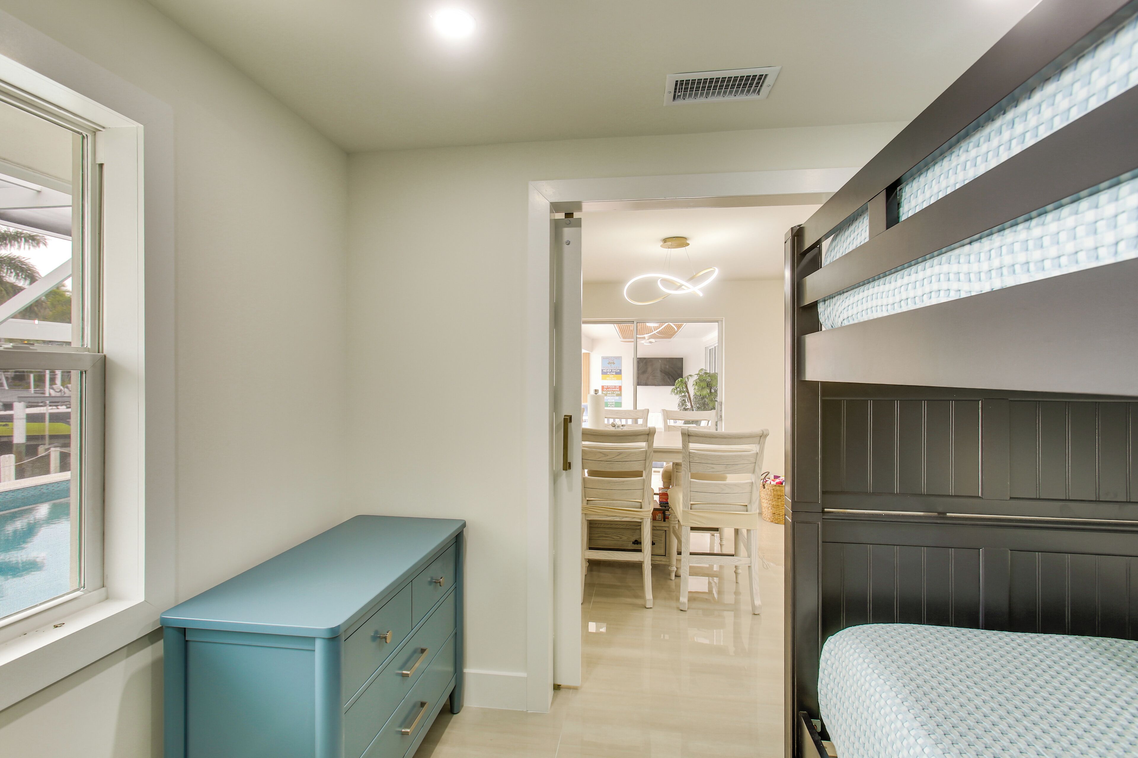 A bedroom with a bunk bed, a dresser, a dining area with chairs, and a neon light.