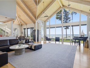 A spacious living room with a large window overlooking the sea, a piano, and a cozy seating area. - Bayview 2.0 | an ESVR property (Wittman)