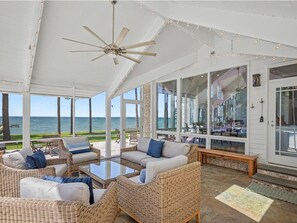 A covered outdoor seating area with wicker furniture, a ceiling fan, and a view of the ocean. - Bayview 2.0 | an ESVR property (Wittman)