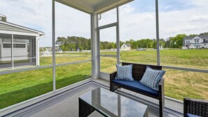 En inglasad uteplats med ett glasbord och en soffa av rotting med kuddar.