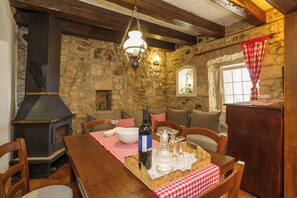 Ein rustikales Steininterieur mit Holztisch, Stühlen, einer Weinflasche und einem Kamin.