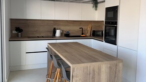 Moderni keittiö, jossa on valkoiset kaapit, puinen keittiösaareke baarituoleineen ja integroidut kodinkoneet.