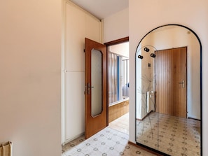 Un pasillo con una puerta de madera, un espejo y suelo de baldosas.