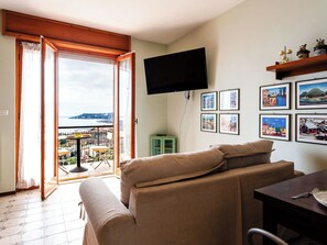 Una sala de estar con sofá, una mesa de comedor, televisor montado en la pared y un balcón con vistas a la ciudad.