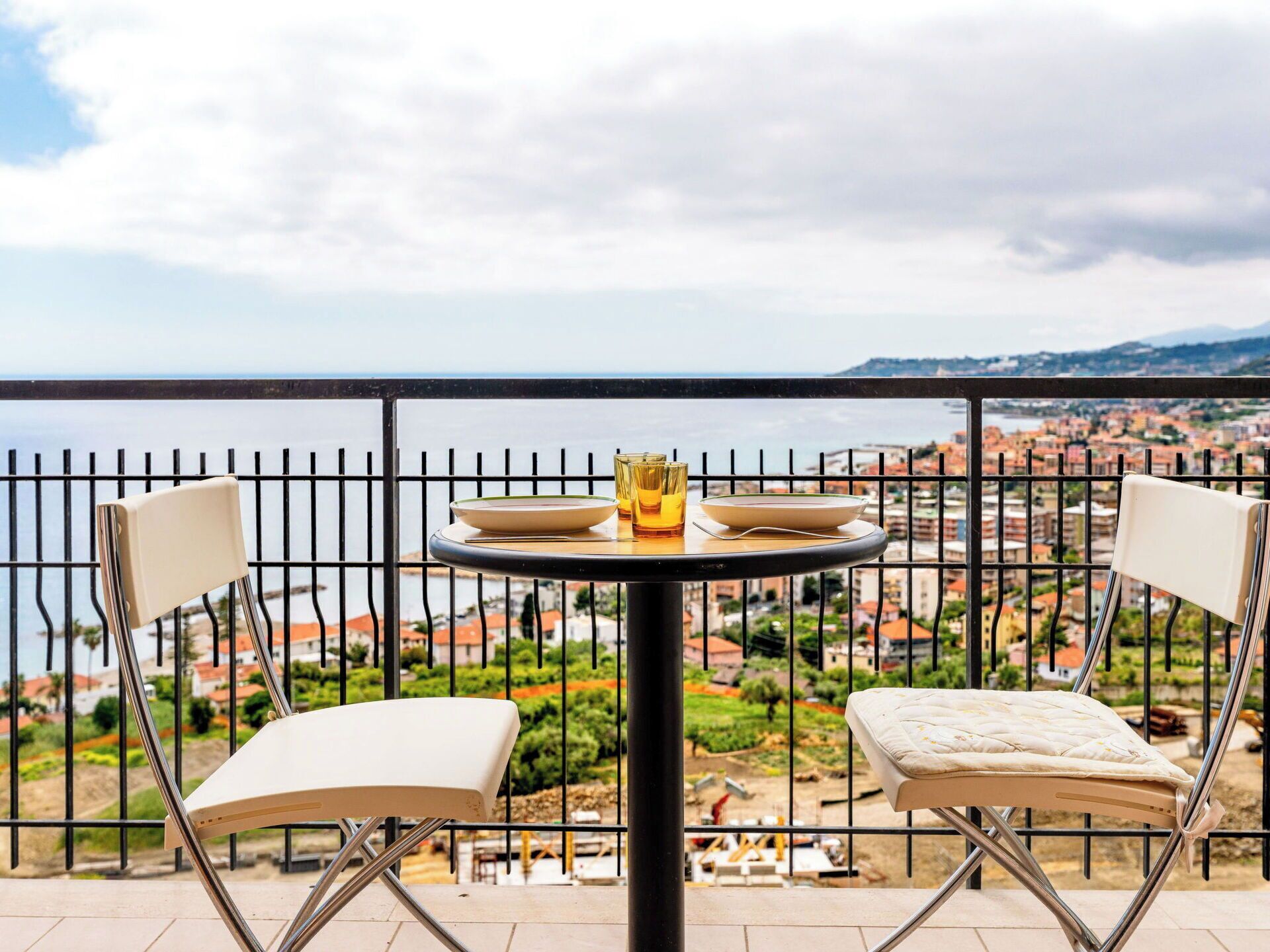 Ein Balkon mit Tisch, zwei Stühlen und Blick auf eine Küstenstadt.