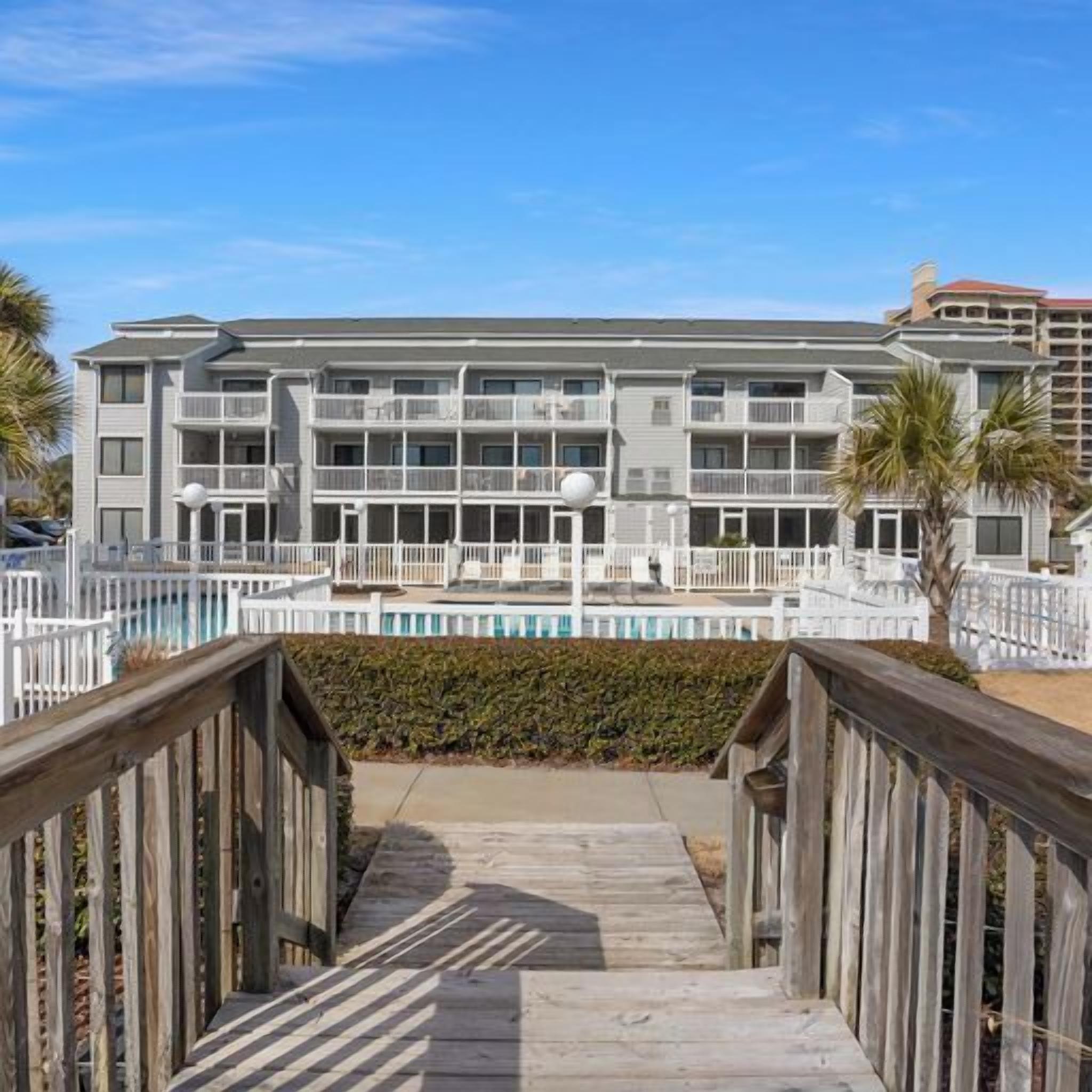 Ein mehrstöckiges Hotel mit Balkonen, einem Pool und einer Holzpromenade, die zum Eingang führt.