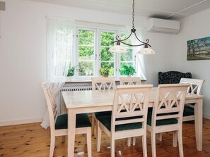 Un comedor con una mesa y sillas blancas, una lámpara colgante, una ventana con cortinas y un cuadro en la pared.