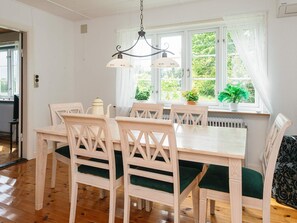 A dining area with a white table and chairs, a hanging light fixture, and a view of greenery through the window. - 6 Person Holiday Home in Rodding (Rodding)