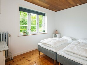 A bedroom with a wooden floor, a bed with white bedding, a window with a view of greenery, and a radiator.