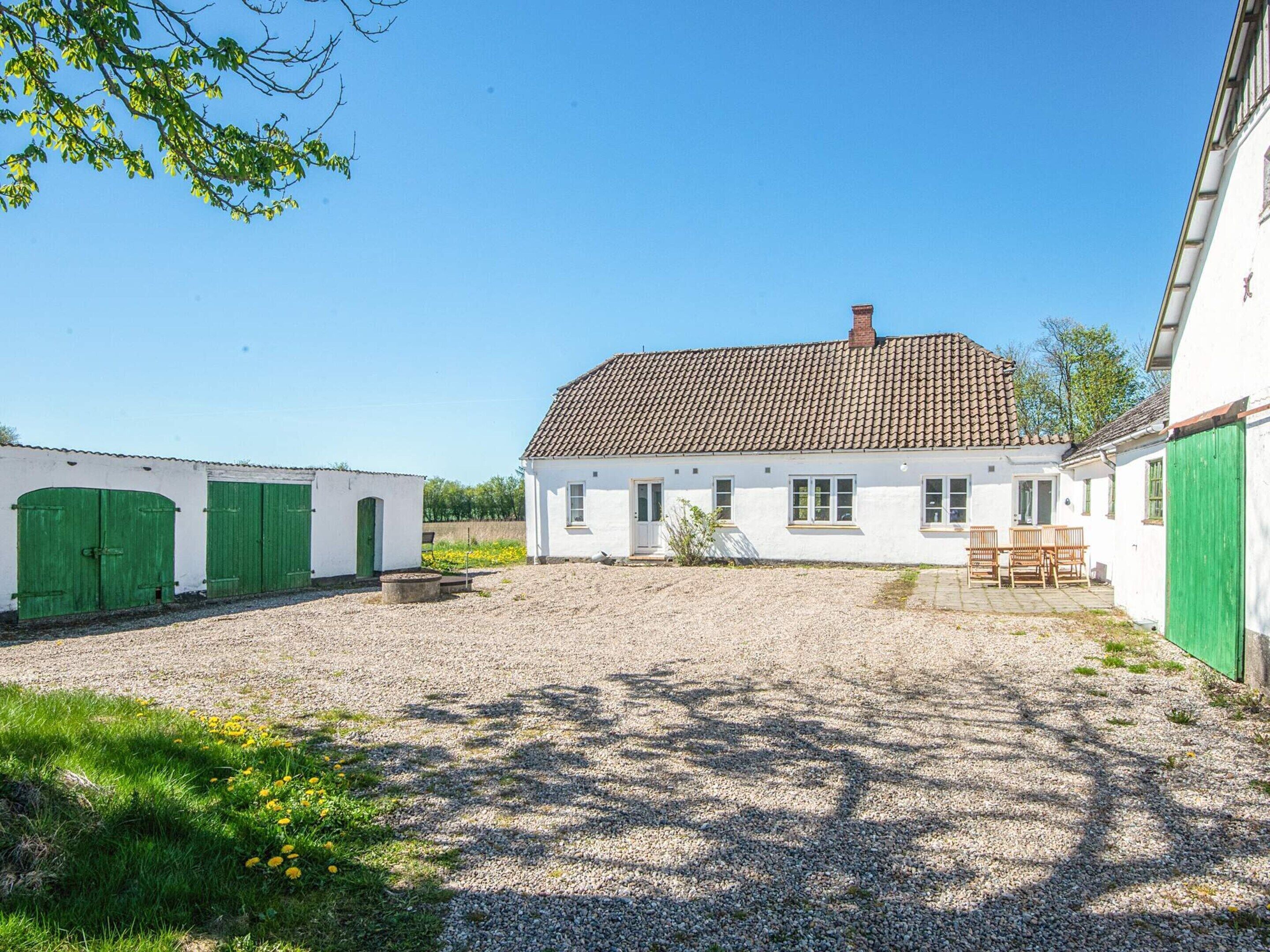 A white building with a tiled roof, green doors, and a gravel courtyard.