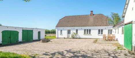 A white building with a tiled roof, green doors, and a gravel courtyard.