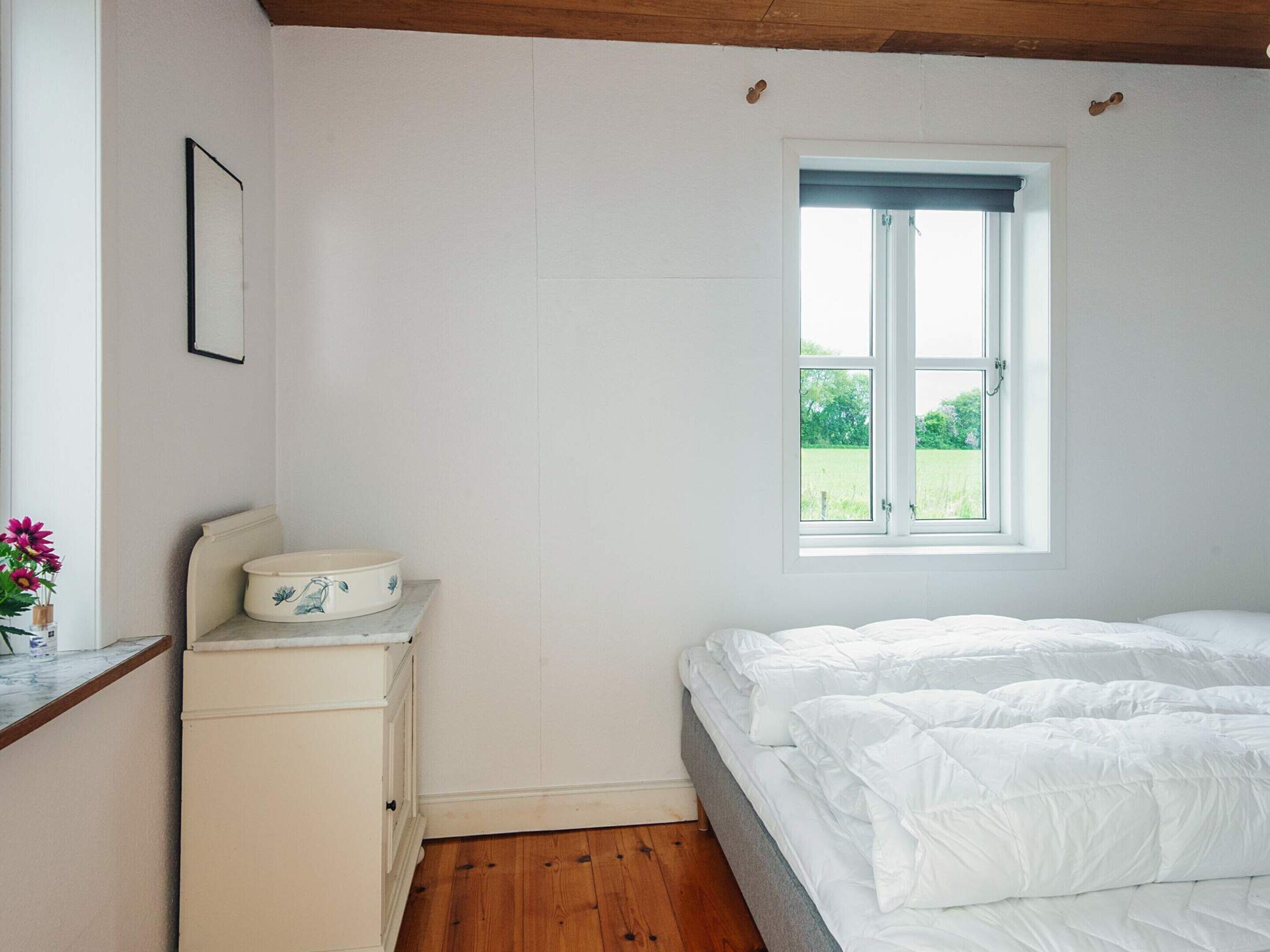 A bedroom with a bed, a window, a dresser, and a framed picture on the wall.