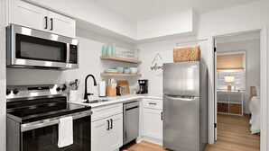 Uma cozinha moderna com eletrodomésticos de aço inoxidável, armários brancos e piso de madeira.