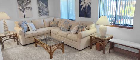 A living room with a sectional sofa, a glass coffee table, a bench, and two lamps.