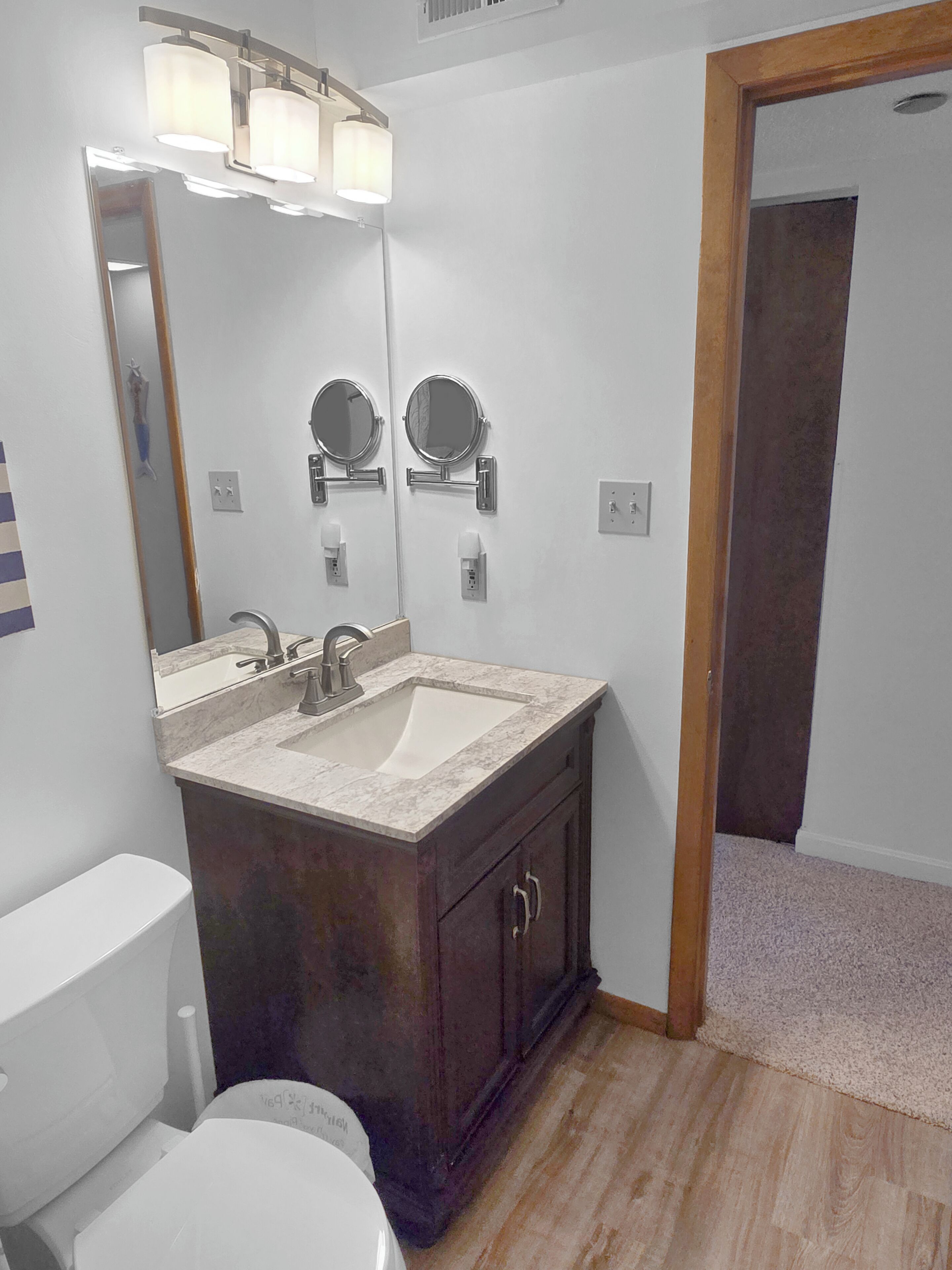 Un baño con lavabo, dos espejos, inodoro y zona de ducha.