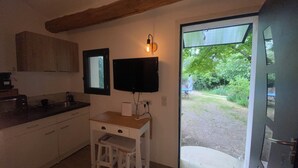 A kitchen with a wooden countertop, a white stool, a wall-mounted TV, and a door leading to a garden.