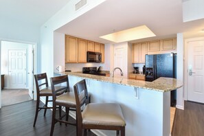 A kitchen with wooden cabinets, a granite countertop, a black microwave, a black refrigerator, and a built-in island with bar stools. - Palms of Destin 21217 by Compass Resorts (Destin)