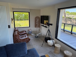 Una habitación con un ventanal grande, un telescopio, un sofá, una silla y una pequeña mesa.