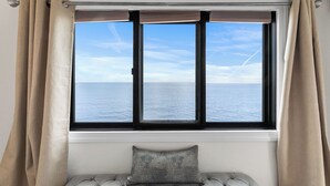 A window with a view of the sea, a cushioned bench, and beige curtains. - Plaza 1612 2bd Oceanfront condo (Ocean City)