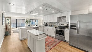 A modern kitchen with white cabinets, stainless steel appliances, and a red patterned rug. - Plaza 1612 2bd Oceanfront condo (Ocean City)