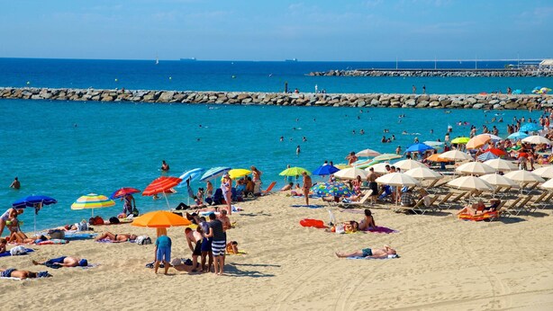 A beach with people sunbathing and swimming, umbrellas, and a rocky breakwater in the background. - Elsi's Place (Premià de Mar)