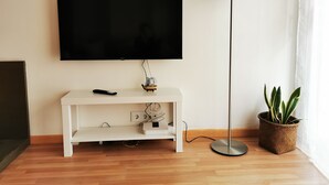 A flat-screen TV mounted on a white console, a floor lamp, and a potted plant. - Elsi's Place (Premià de Mar)
