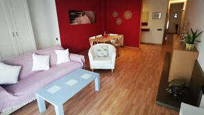 A living room with a sofa, a coffee table, a dining area with chairs, a red accent wall, and a hallway leading to another room. - Elsi's Place (Premià de Mar)