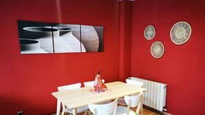 A room with a wooden table and white chairs, red walls, and a radiator. - Elsi's Place (Premià de Mar)