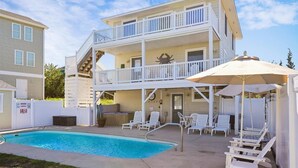 Ein zweistöckiges Gebäude mit Pool, Sitzgelegenheiten im Freien und einer überdachten Terrasse mit Sonnenschirmen.