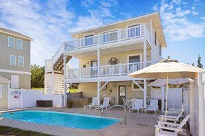 A two-story building with a pool, outdoor seating, and a covered area with umbrellas. - The Blue Crab Cottage -- Back for 2026 Pool, Hot Tub and More! (Duck)