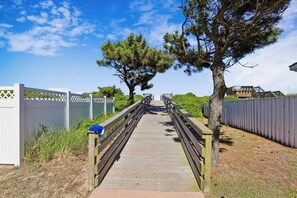 A wooden boardwalk leading to a building with a white fence on one side and a metal fence on the other. - The Blue Crab Cottage -- Back for 2026 Pool, Hot Tub and More! (Duck)