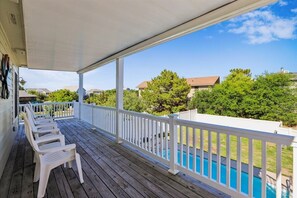 A covered outdoor area with a pool, white railings, and a row of white plastic chairs. - The Blue Crab Cottage -- Back for 2026 Pool, Hot Tub and More! (Duck)