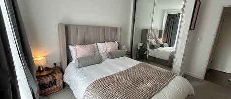 Een slaapkamer met een bed, nachtkastje, lamp, spiegel en uitzicht.