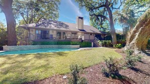 A house with a swimming pool, a covered patio, and a large tree in the foreground. - 15 Rum Row: 3  BR, 3  BA House in Hilton Head Island, Sleeps 6 (Hilton Head Island)