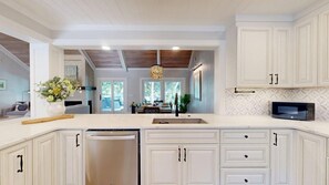 A kitchen with white cabinetry, a dishwasher, a microwave, and a dining area with a chandelier. - 15 Rum Row: 3  BR, 3  BA House in Hilton Head Island, Sleeps 6 (Hilton Head Island)