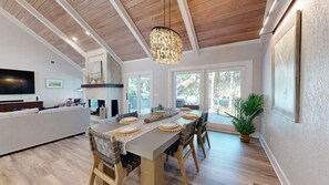 A spacious dining area with a long table set for four, a chandelier, and a view of the outdoors. - 15 Rum Row: 3  BR, 3  BA House in Hilton Head Island, Sleeps 6 (Hilton Head Island)