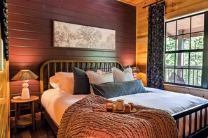 Ein Zimmer mit Holzwänden, einem Bett, einem Tisch mit Lampe und einem Fenster mit Vorhängen.