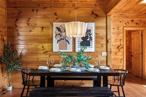 Een houten interieur met een eettafel gedekt voor vier personen, twee ingelijste kunstwerken aan de muur en een potplant.