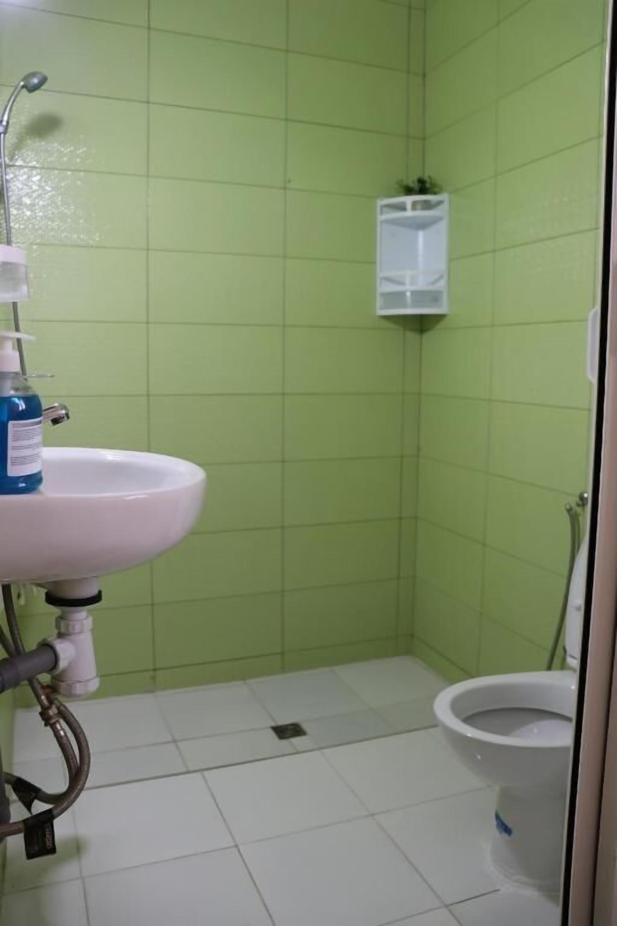 Un baño con un lavabo blanco, paredes de azulejos verdes, un inodoro blanco y un pequeño estante blanco.