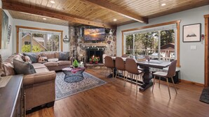 A spacious living room with a stone fireplace, wooden ceiling, and large windows. - Cozy Bear Lodge (Big Bear City)