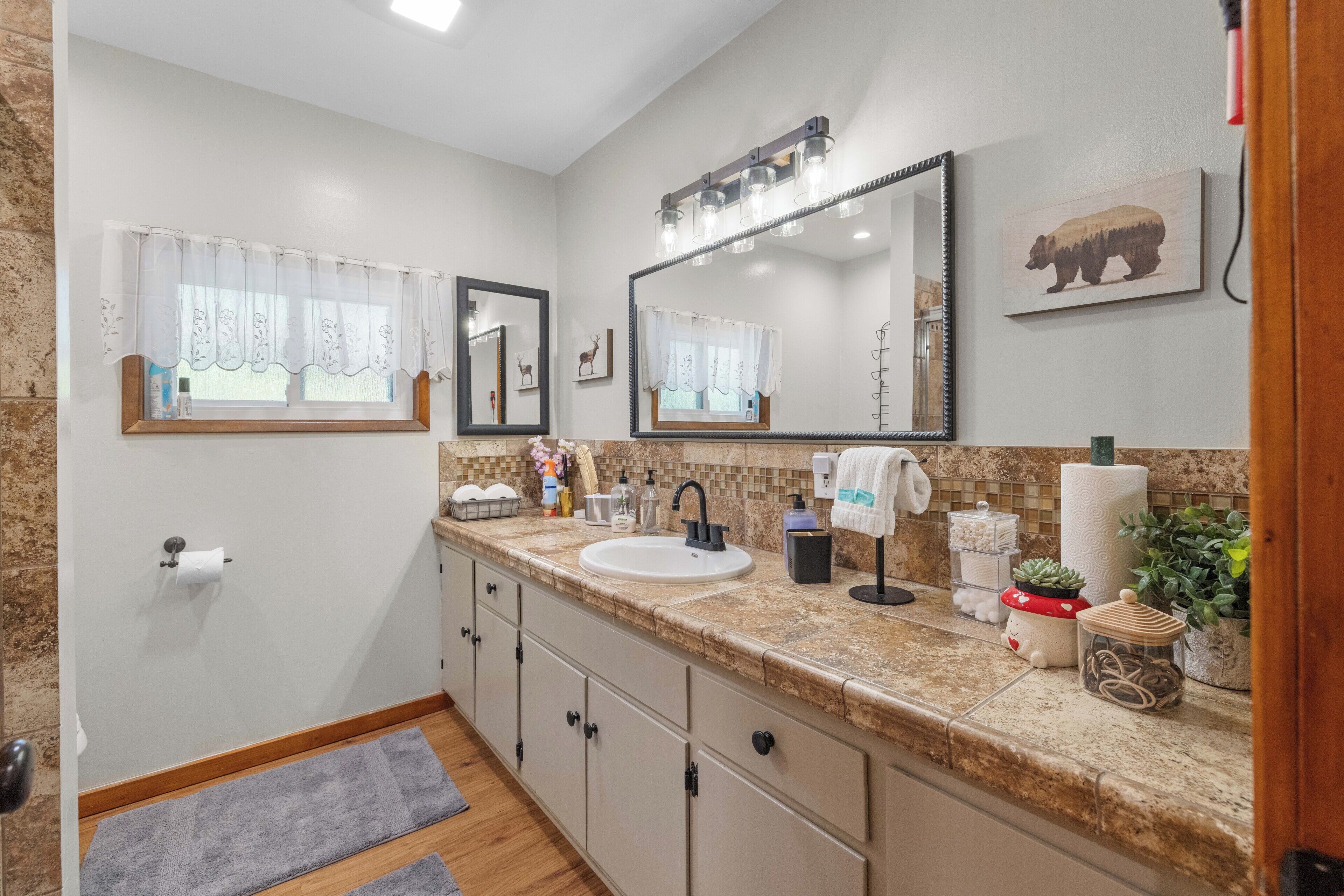 A bathroom with a sink, mirror, vanity, and a window with a curtain.