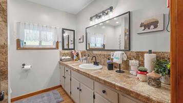 A bathroom with a sink, mirror, vanity, and a window with a curtain.