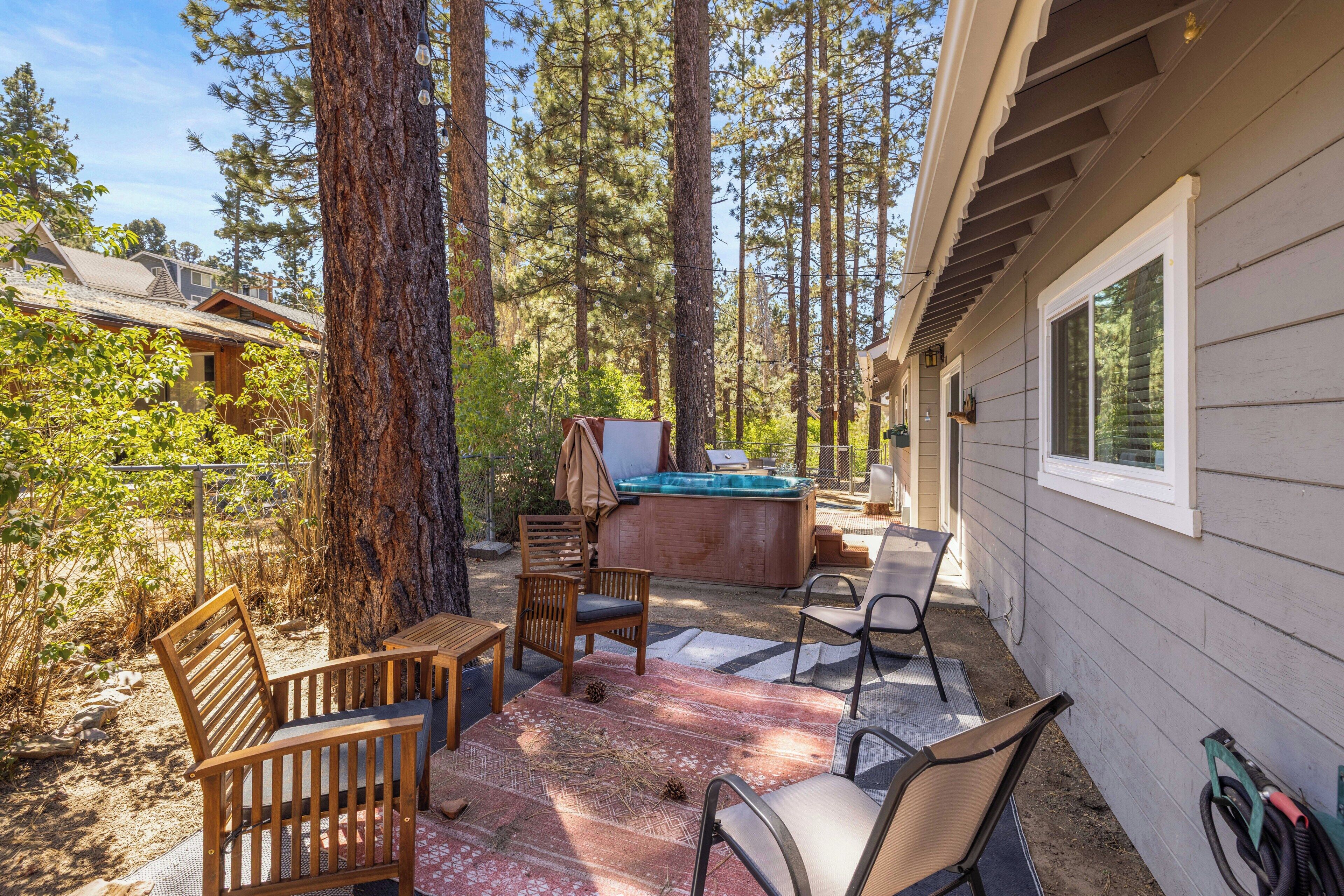 A cabin with a hot tub, wooden chairs, and a patio area surrounded by tall trees.