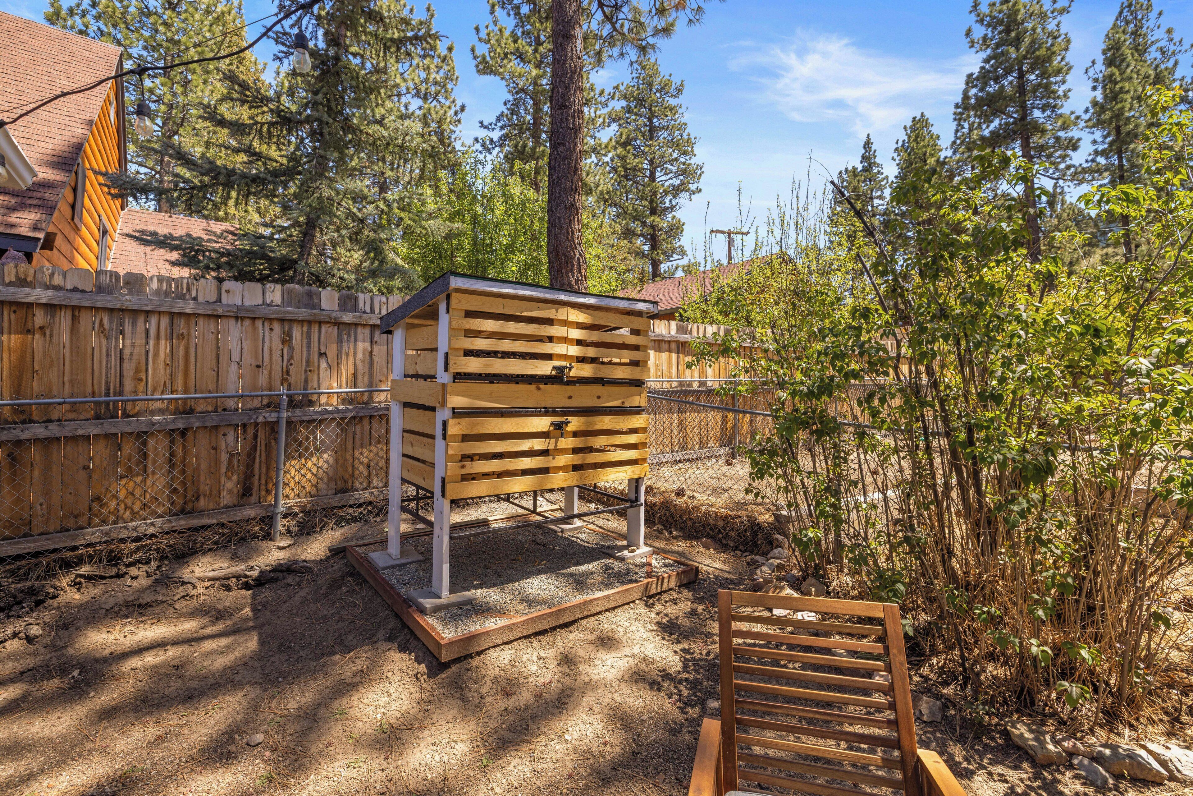 A wooden structure with a metal frame, possibly a shed or storage unit, in a backyard with a wooden fence, trees, and a bench.