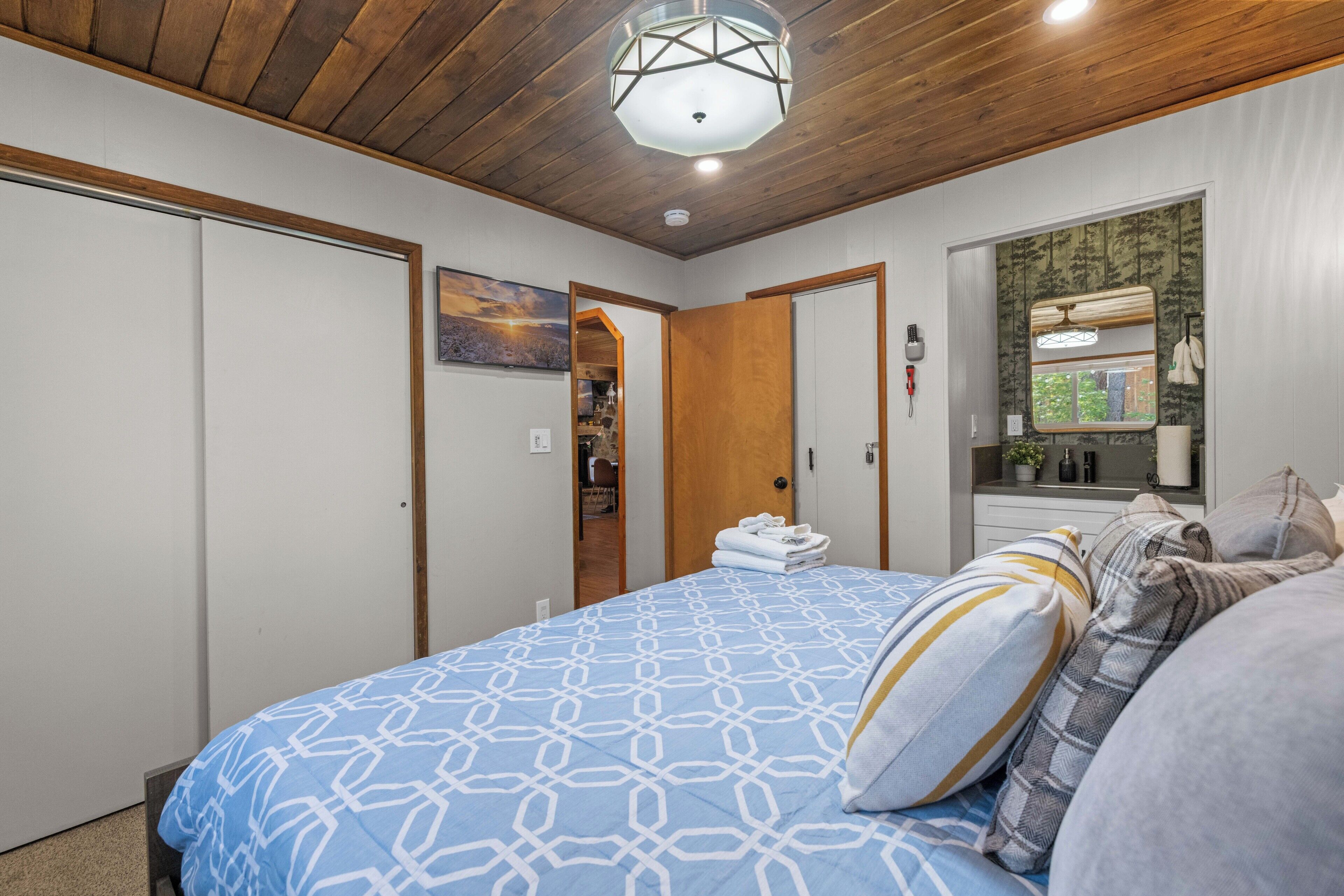 Un dormitorio con techo de madera, una cama grande con ropa de cama estampada, un armario y un espejo con vistas.
