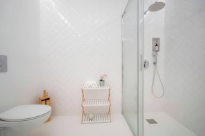 Une salle de bain équipée de toilettes, d’une douche et d’une étagère où sont posées des serviettes et une plante.